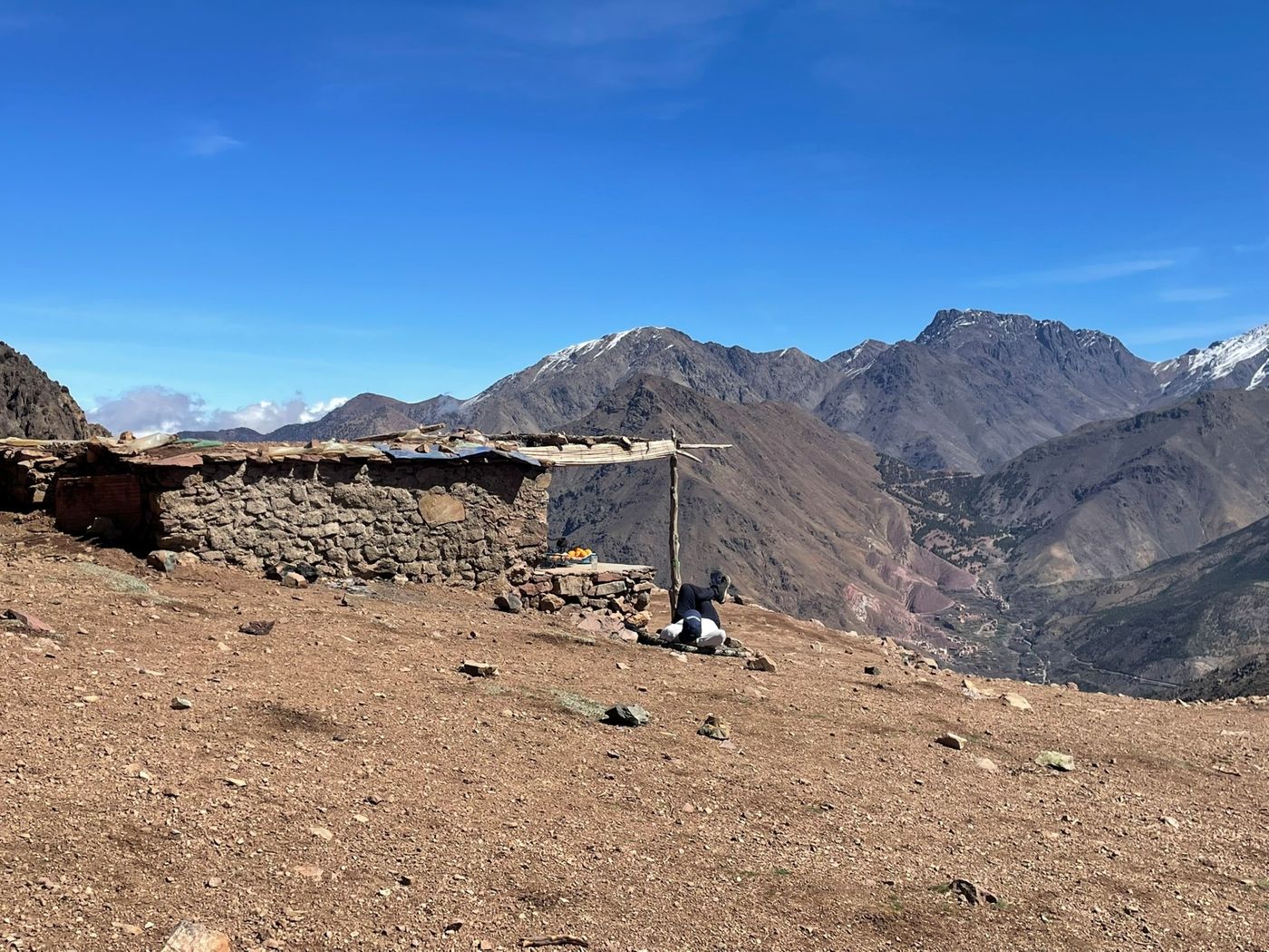Hiker resting next to a rustic stone shelter that overlooks the High Atlas Mountains of Morocco.